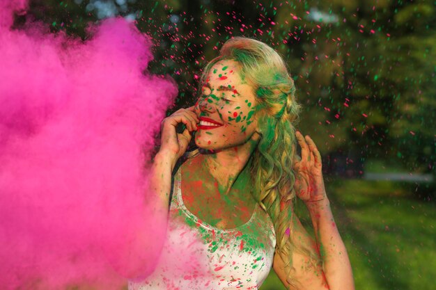 Aanbiddelijk Kaukasisch model met krullend haar poserend in een wolk van roze droge verf, ter ere van Holi-festival