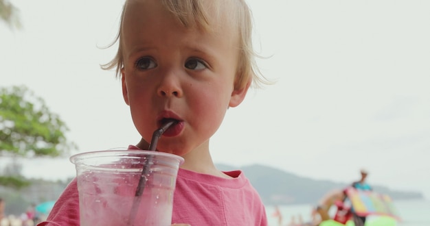 Aanbiddelijk klein jong geitje dat koude drank drinkt en weg terwijl status kijkt