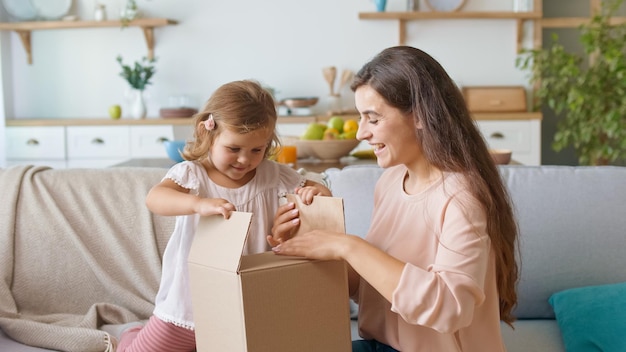 Aanbiddelijk meisje dat de bestelling uitpakt Gelukkige moeder en dochter die de bestelling uitpakt die een jong meisje v...