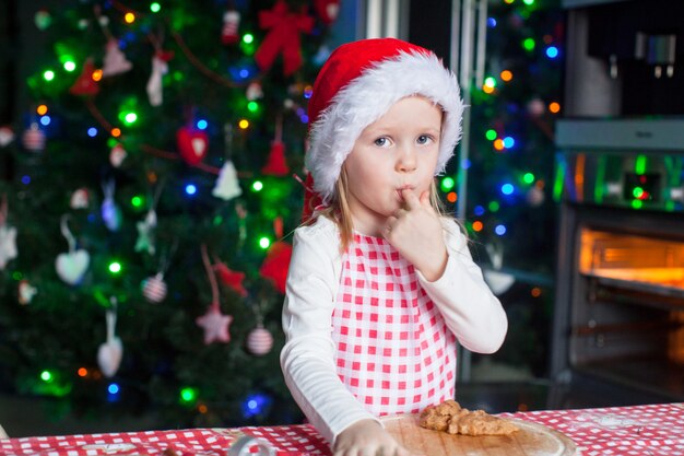 Aanbiddelijk meisje dat in Kerstmanhoed het deeg voor gemberkoekjes eet