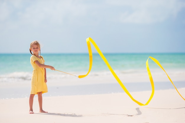 Aanbiddelijk meisje dat met geel gymnastieklint op het strand danst