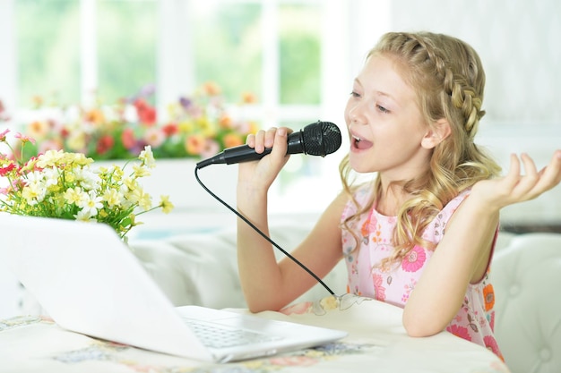 Aanbiddelijk meisje dat moderne laptop gebruikt en karaoke zingt