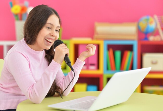 Aanbiddelijk meisje dat moderne laptop gebruikt en karaoke zingt