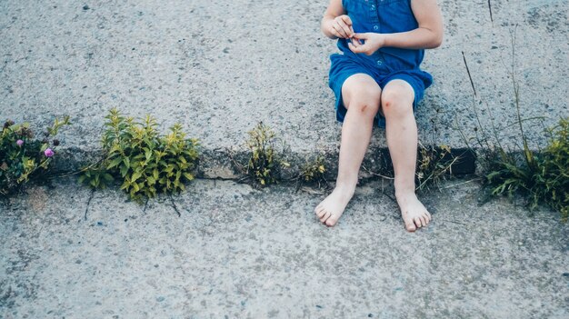 Aanbiddelijk meisje dat op aard lacht - gelukkig meisje in een blauwe jurk en door de knieën geslagen zit op de trap. gelukkige jeugd.