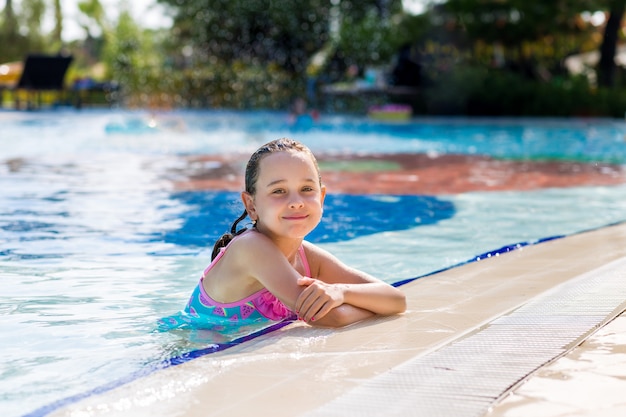 Aanbiddelijk meisje in helder zwempak in zwembad op vakantie op zonnige de zomerdag. Familie vakantie concept