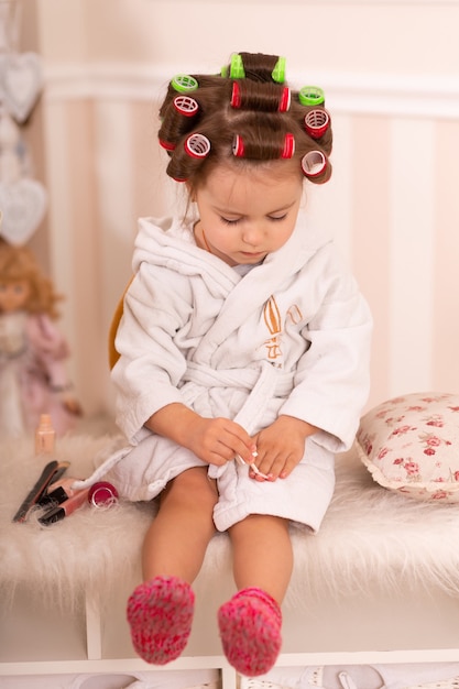 Aanbiddelijk meisje met krulspelden schildert haar vingernagels. kopieert het gedrag van mama. jonge fashionista. schoonheid dag.