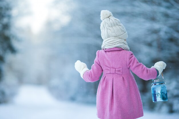 Aanbiddelijk meisje met lamp en kaars in de winter op Kerstmisvooravond in openlucht