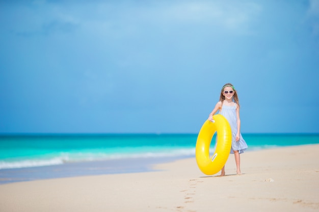 Aanbiddelijk meisje met opblaasbare rubbercirkel op wit strand klaar om te zwemmen