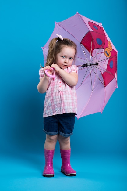 Aanbiddelijk meisje met roze paraplu op blauwe achtergrond