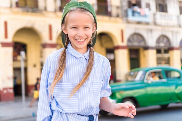 Foto aanbiddelijk meisje op populair gebied in oud havana, cuba. portret van jong geitje uitstekende klassieke amerikaanse auto als achtergrond