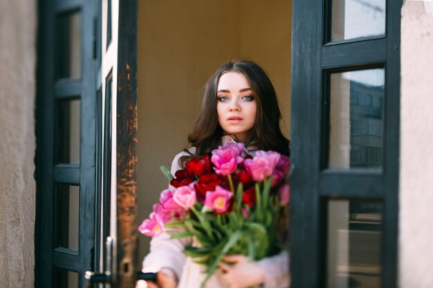 Aanbiddelijk modieus portret van de schuine standverschuiving van gelukkig glimlachend donkerbruin meisje met boeket van tulpen