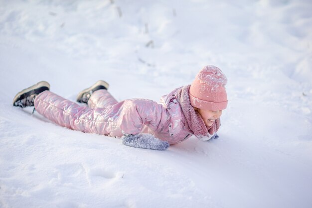 Aanbiddelijk weinig gelukkig meisje die in de winter sneeuwdag rodelen.