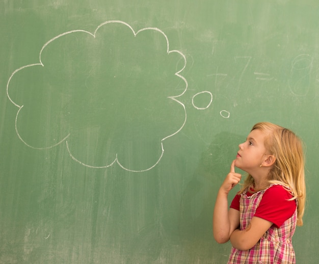 Aanbiddelijk weinig meisje van het schoolblonde in schoolklaslokaal aan boord van het stellen met wolk voor exemplaarruimte