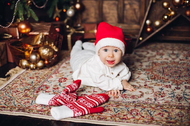 Aanbiddelijke gelukkige baby in rode hoed op tapijt met leuke de winterwanten.