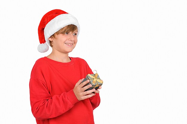 Aanbiddelijke glimlachende blonde jongen draagt een rode kerstmuts en rode trui en wacht op een nieuwe