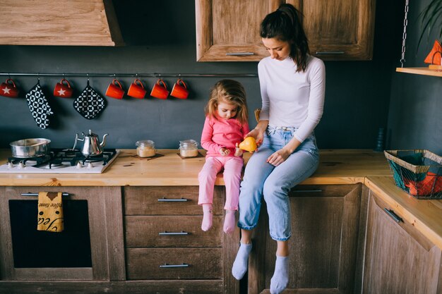 Aanbiddelijke jonge vrouw die met haar kleine grappige dochter in keuken speelt.