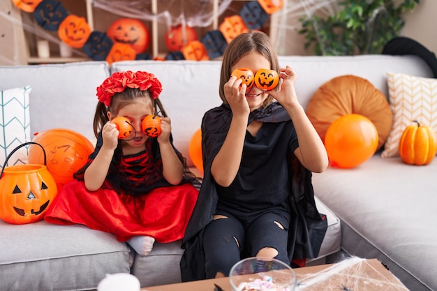 Aanbiddelijke jongen en meisje die Halloween-kostuum dragen die pompoenmanden over ogen thuis houden