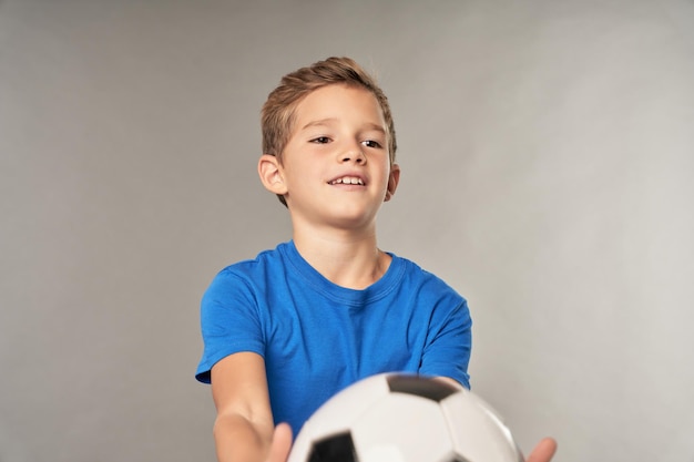 Aanbiddelijke jongen met voetbal die zich tegen grijze achtergrond bevindt