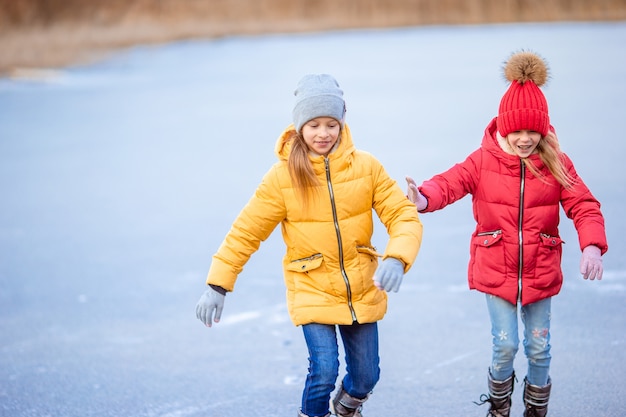 Aanbiddelijke meisjes die op ijsbaan in openlucht in de dag van de de wintersneeuw schaatsen