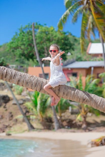 Aanbiddelijke meisjezitting op palm tijdens de zomervakantie op wit strand