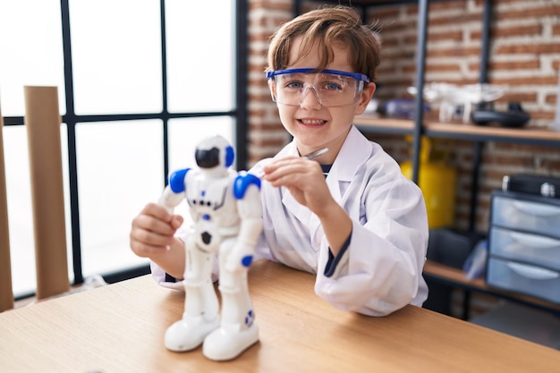 Aanbiddelijke Spaanse jongen student glimlachend zelfverzekerde reparerende robot in laboratorium klaslokaal