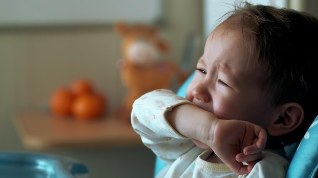 Aanbiddelijke trieste blanke baby die huilt in een kinderstoel in de keuken