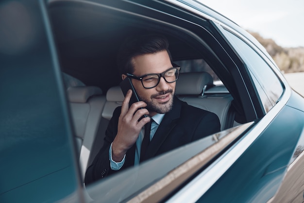 Aangenaam gesprek. Doordachte jonge zakenman die aan de telefoon praat terwijl hij in de auto zit