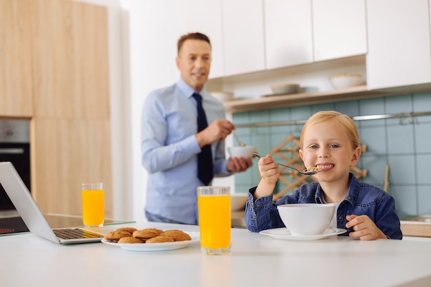 Aangenaam leuk jong meisje, zittend aan tafel en met een lepel