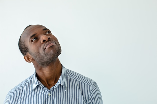 Aangename Afro-Amerikaanse man die betrokken is bij gedachten terwijl hij tegen een witte muur staat