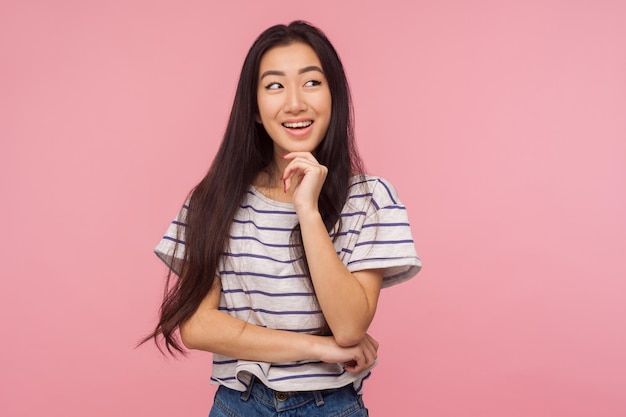 Aangename herinneringen. Portret van een meisje met lang haar in een gestreept t-shirt dat lacht en iets aangenaams droomt, fantasie bewondert, nadenkt over een goed idee. indoor studio-opname geïsoleerd op roze achtergrond