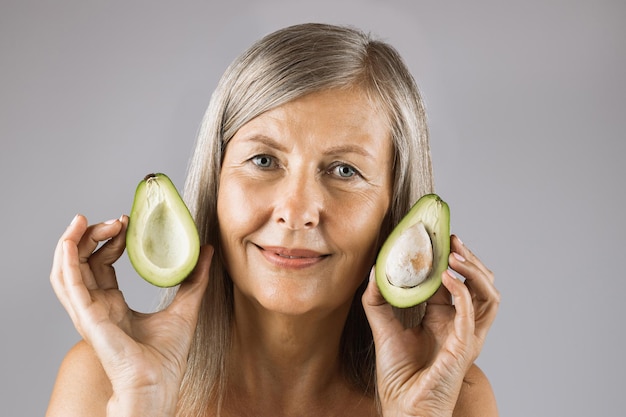 Aangename rijpe vrouw met helften van groene rijpe avocado