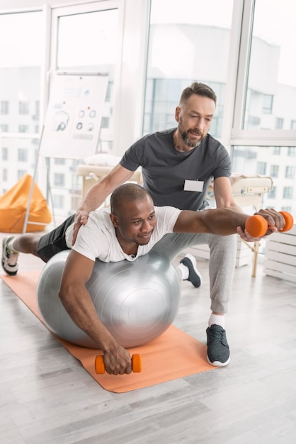 Aangename training. Vrolijke aardige positieve man die lacht terwijl u geniet van de fysieke training