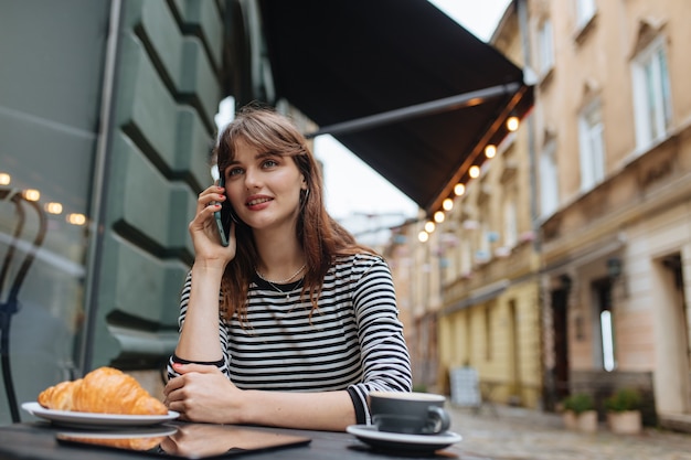 aangename vrouw in casual outfit ontspannen in gezellig café met lekkere koffie en een verse croissant