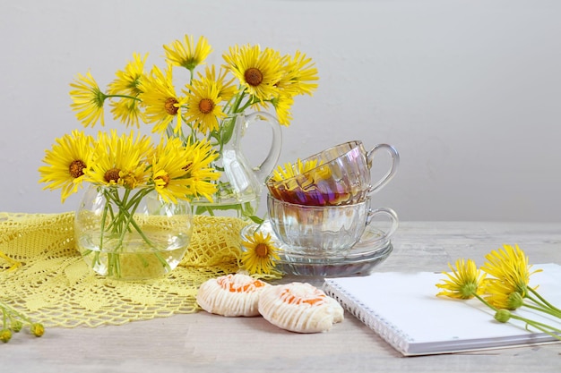 Aangename zomer theekransje een kopje thee met gele kamille boeketten van gele bloemen op een grijze achtergrond Kladblok koekjes ruimte voor tekst