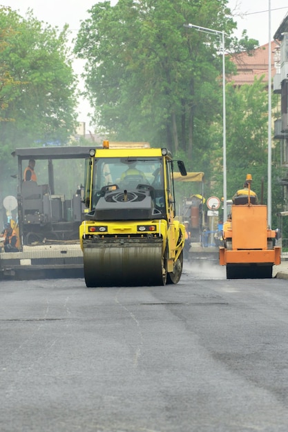 Aanleggen van nieuw asfalt op een stadsstraat Grote apparatuur voor het leggen en aanstampen van asfalt werkt op de weg Het gebruik van een wals bij het leggen van asfalt zorgt voor een absolute gelijkmatigheid van de coating