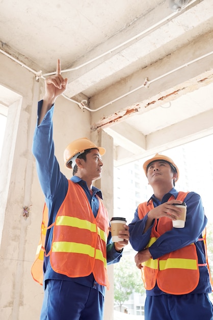 Aannemers die 's ochtends koffie drinken en plafondplaten en bedrading bespreken in het huis in aanbouw