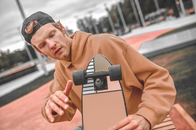 Aanpassing, skateboard. Geconcentreerde roodharige man die een skateboard vasthoudt en de draaiende vingers van het wiel aanraakt terwijl hij overdag in het park zit