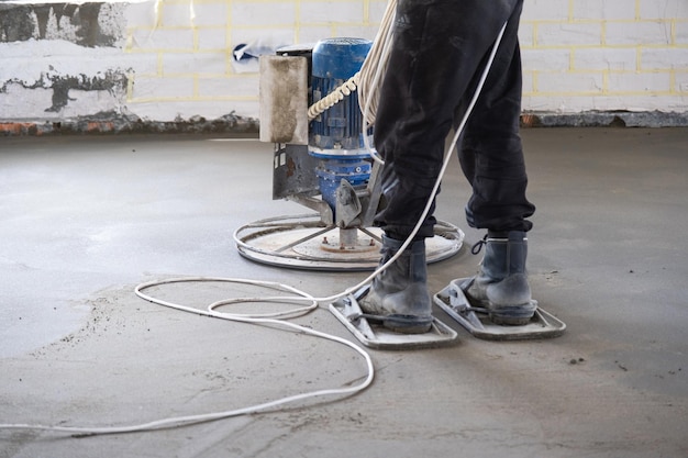 Aanstampen en slijpen van halfdroge dekvloer door een machine met een roterende schijf voor het egaliseren Bouw van een betonnen vloer in het huis een meester met speciale apparatuur