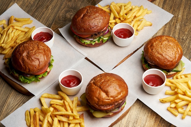 Aantal hamburgers met frietjes en ketchupsaus. Grote hamburgers en frietjes op houten tafel achtergrond. Fastfood achtergrond instellen. Restaurant hamburgermenu