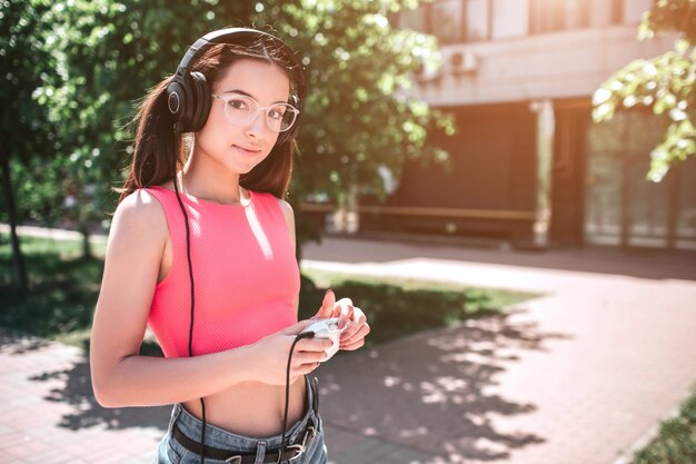 Aantrekkelijk en geweldig meisje kijkt en poseren. Ze luistert naar muziek in een koptelefoon. Ook houdt het meisje witte speler in haar handen. Ze staat op straat.