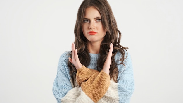 Aantrekkelijk ernstig donkerbruin meisje in sweater die geen gebaar met gekruiste handen op camera tonen over witte achtergrond