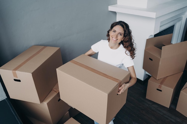 Aantrekkelijk europees meisje in witte t-shirt die het huis verlaat Dame die kartonnen dozen inpakt en draagt