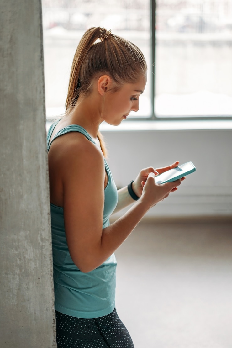 Aantrekkelijk fit jonge vrouw lichtblauwe sportkleding training met mobiel bij binnenlandse training klasse loft studio, fitness gezonde levensstijl