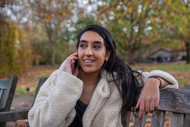 Aantrekkelijk Indisch meisje zittend op een bankje in een park in Londen met een telefoontje