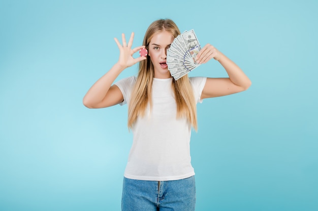 Aantrekkelijk jong blondemeisje met pookspaander van online casino en geld dat over blauw wordt geïsoleerd