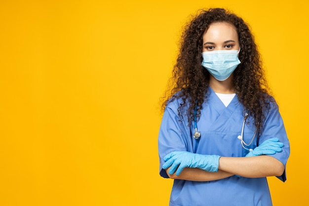 Aantrekkelijk jong meisje in een blauw verpleegsteruniform en een masker op een gele achtergrond