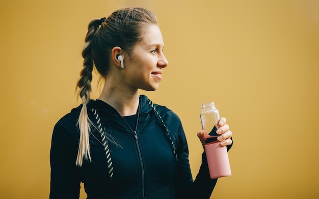 Aantrekkelijk kaukasisch meisje op gele geïsoleerde achtergrond met draadloze koptelefoon in sportpak laat training rennen en drinkwater