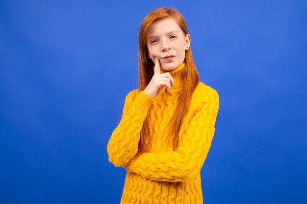 Aantrekkelijk Kaukasisch roodharig meisje in een gele sweater die op blauw redeneert