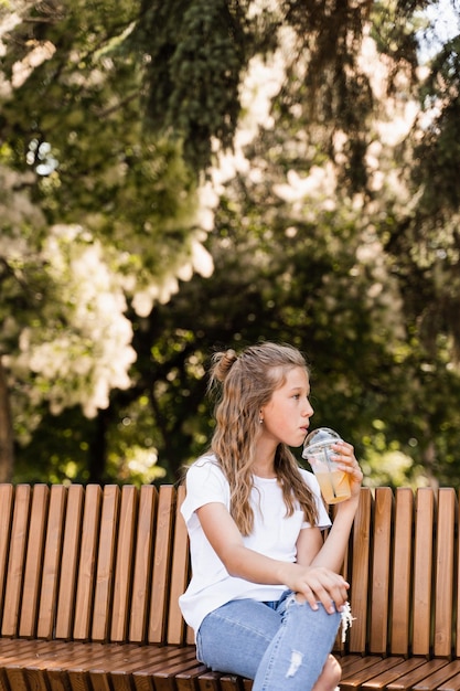 Aantrekkelijk kindmeisje dat zomerlimonade drinkt Zomercocktails Gelukkig meisje met beker met sinaasappellimonade buiten