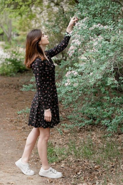 Aantrekkelijk meisje dat in een bloeiende tuin staat en bloesem aanraakt en bewonderend opkijkt